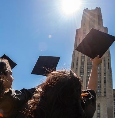 Students wearing graduation gowns hold their graduation caps up towards the sky