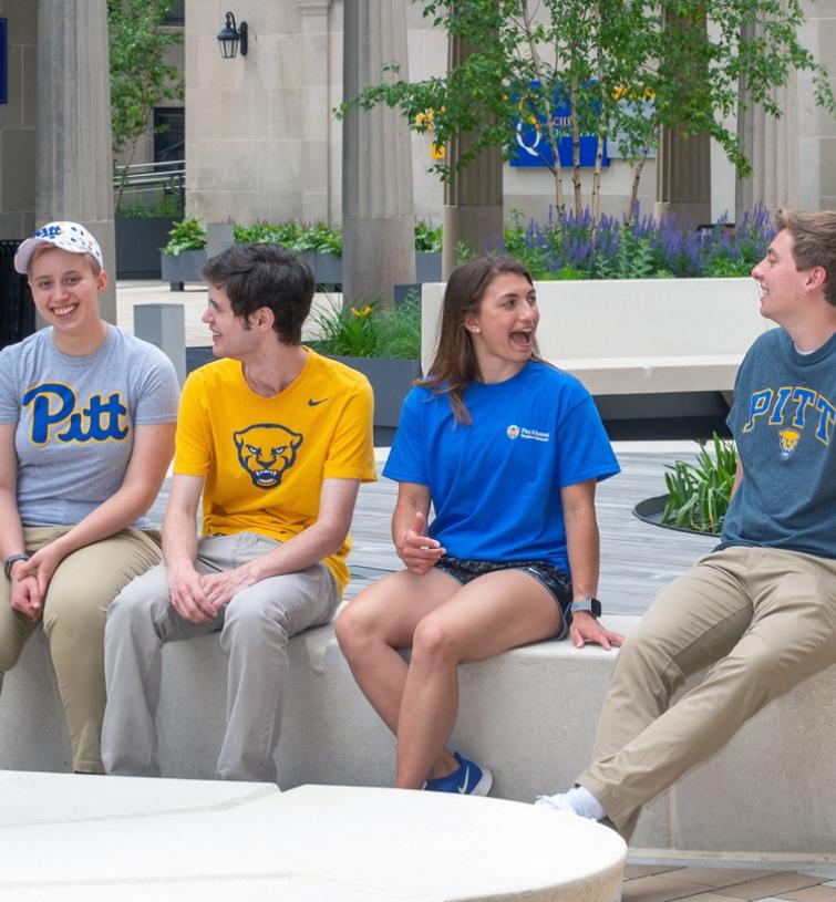 Four students wearing Pitt shirts sit on a concrete platform
