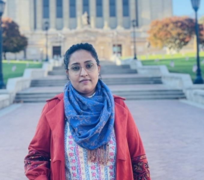 Rashmi Sheila-Dangol standing in front concrete steps and a building with pillars